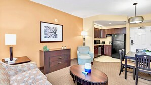 A hotel room with a sofa, a small table, a lamp, a chair, a kitchenette, and a dining area. - Condo 1BR Near Disney- Pool and Hot Tub! (Orlando)