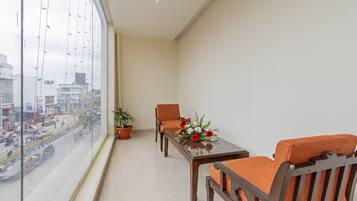 A balcony with a view of a cityscape, a potted plant, a wooden table, and two chairs with orange cushions.