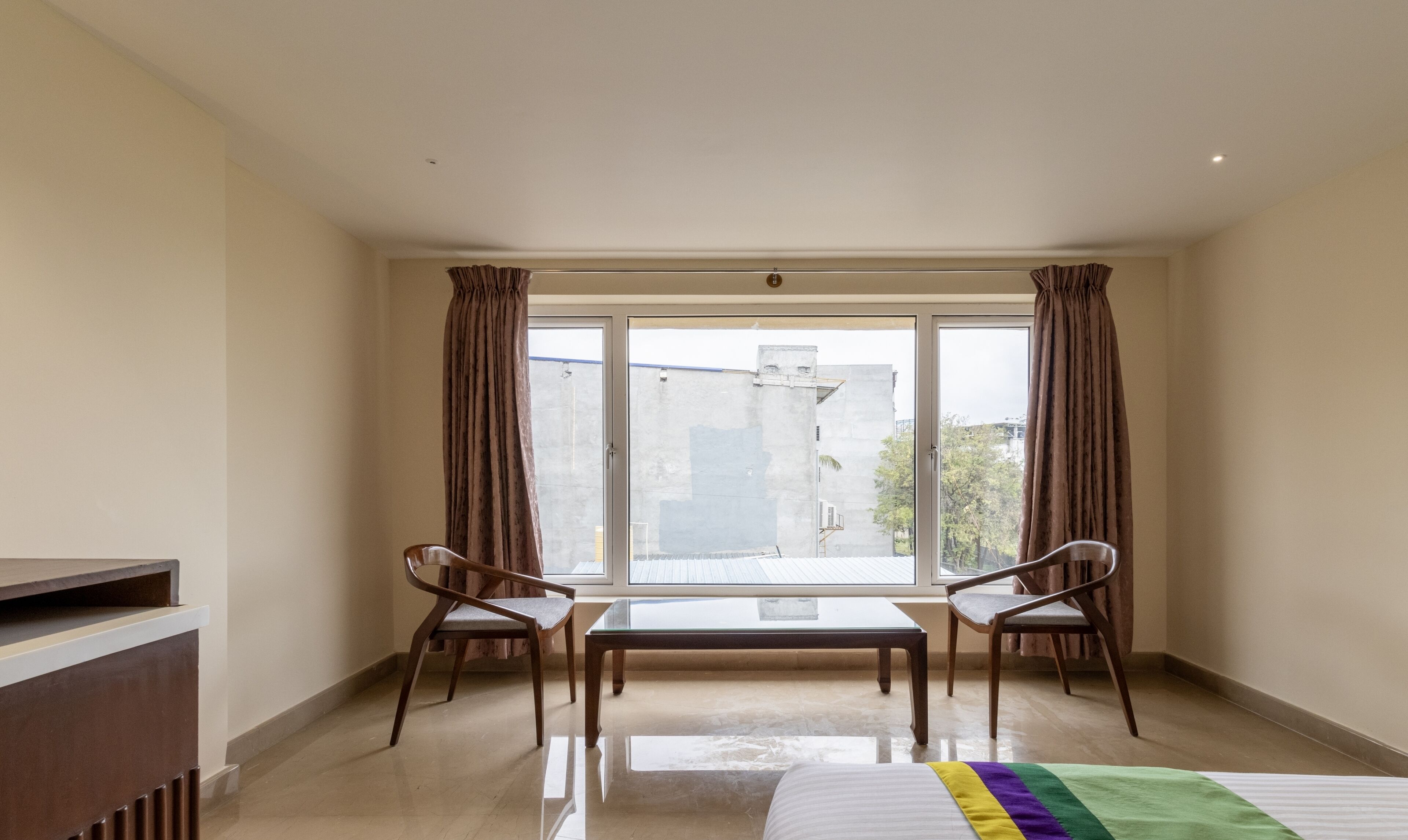 A hotel room with a large window, two chairs, a bed, and a radiator.