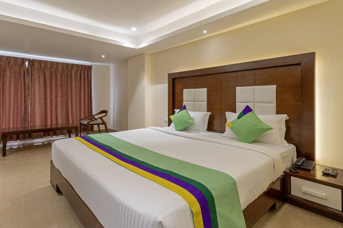 A hotel room with a large bed, a wooden headboard, a bedside table with a phone, and a chair.