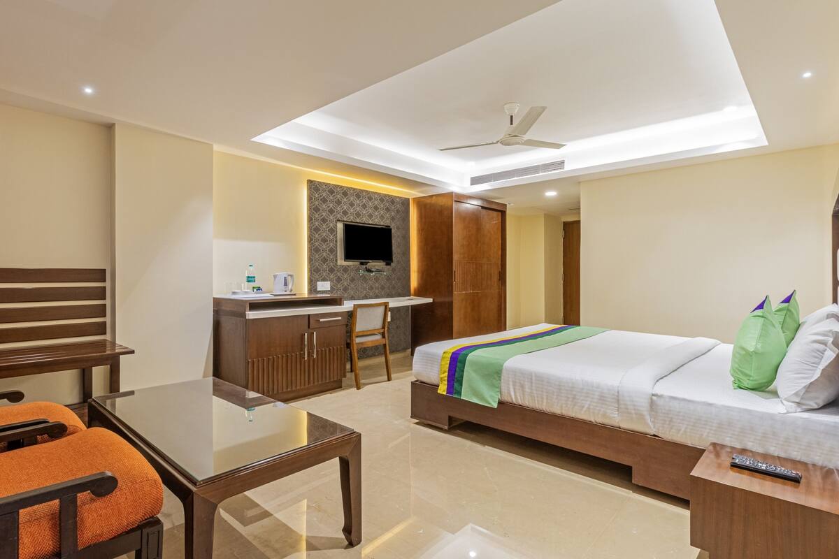A hotel room with a bed, a desk, a chair, a TV, and a ceiling fan.