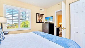 Une chambre à coucher avec un lit, une commode, un téléviseur et une fenêtre avec des stores.