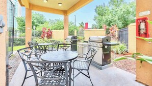 An outdoor patio area with a round table and chairs, a grill, and a trash can. - Condo Near Universal Studios With Pool & Hot Tub (Orlando)