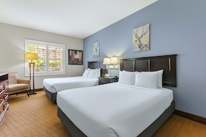 A hotel room with two beds, a desk, a chair, and a window with blinds.