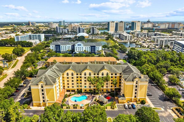 Un grand hôtel doté d’une piscine, entouré de verdure, avec une vue sur la ville en arrière-plan.