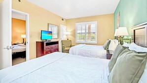 Ein Hotelzimmer mit zwei Betten, einem Fernseher, einem Schreibtisch und einem Sessel.