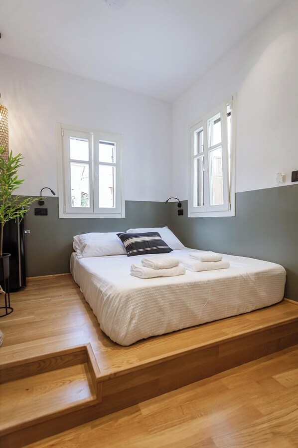 A bedroom with a bed, two windows, a plant, and a staircase.