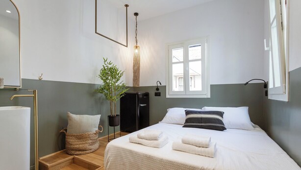 Une chambre d’hôtel bien rangée, avec un lit, une table de chevet, une lampe et une fenêtre.