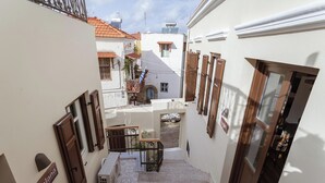 Une ruelle étroite avec un escalier menant à une porte, un petit espace extérieur aménagé avec des sièges et une enseigne sur le mur.