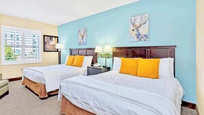 Une chambre d’hôtel avec deux lits, une fenêtre avec des stores, une table de chevet et des œuvres d’art accrochées aux murs.