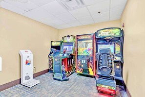A row of arcade games in a hallway with a scale for weighing luggage.