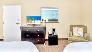 A hotel room with two beds, a dresser, a coffee maker, a lamp, a painting, and a chair with a polka dot pillow.
