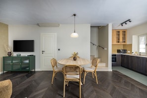 Een eethoek met een ronde tafel en stoelen, een televisie, een kast en een trap naar een keuken.
