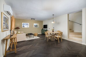 Ein Wohnzimmer mit einer Couch, einem Esstisch mit Stühlen, einem Fernseher und einer Treppe.