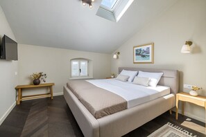 Ein Schlafzimmer mit einem Bett, einem Nachttisch, einem kleinen Fenster, einem an der Wand befestigten Fernseher und einer Deckenleuchte.