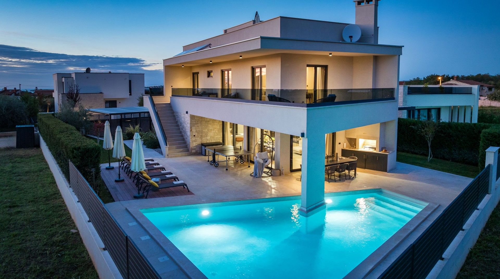 A modern two-story house with a swimming pool, outdoor seating, and a staircase leading to the upper level.