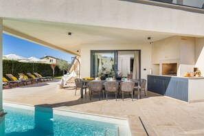 A modern outdoor dining area with a pool, lounge chairs, and a hanging chair.