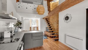 Une cuisine moderne dotée d’un îlot central, d’un escalier en bois et d’une horloge murale aux motifs géométriques.