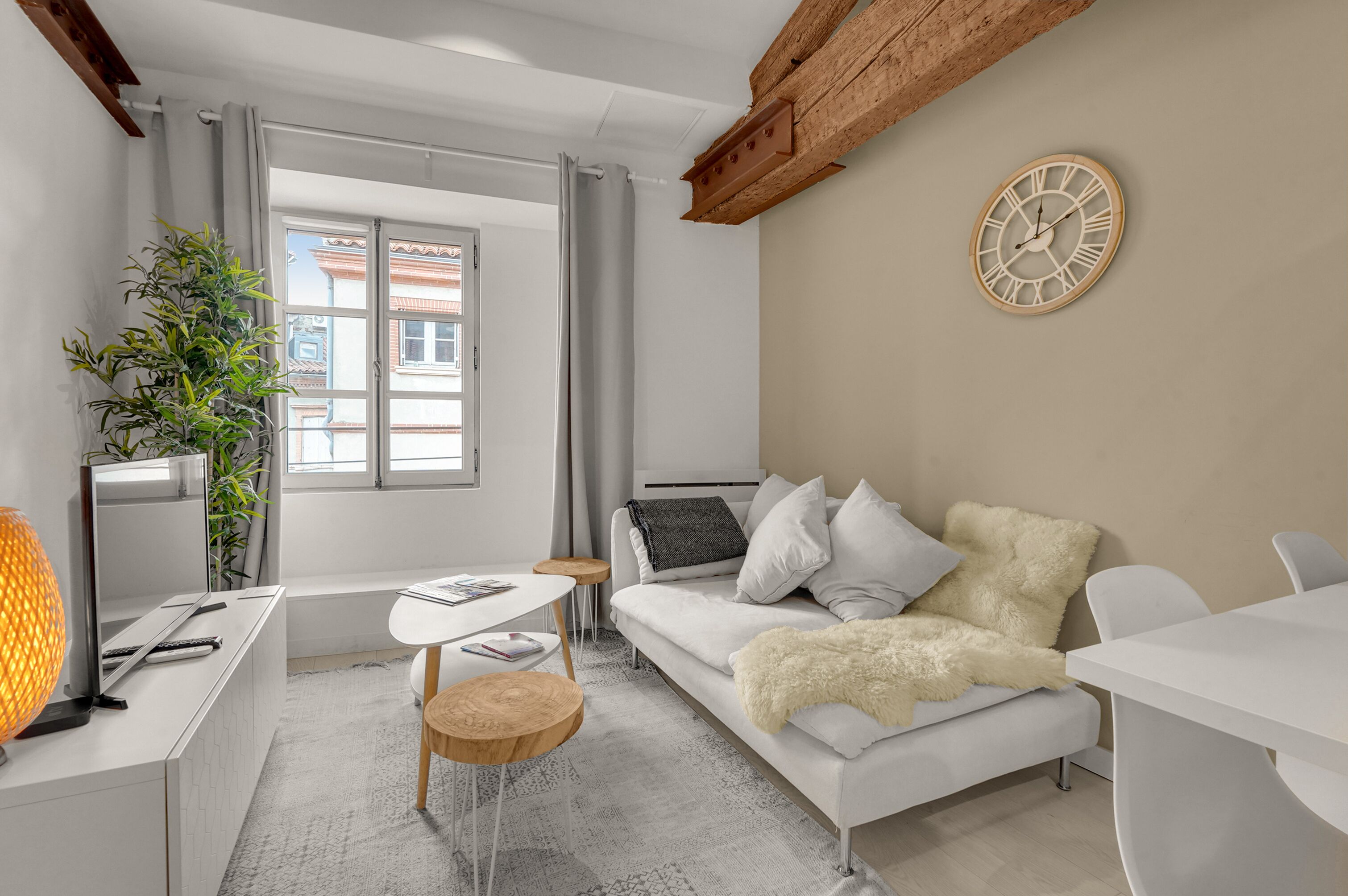 A modern living room with a white sofa, a small wooden table, a TV, and a large window with curtains.