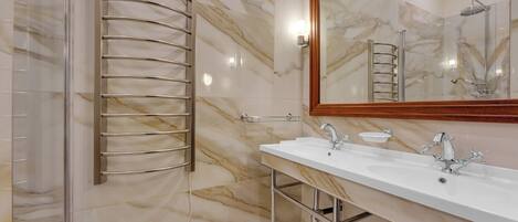 A modern bathroom with a glass shower enclosure, a marble-tiled wall, a double sink with chrome fixtures, and a large mirror.