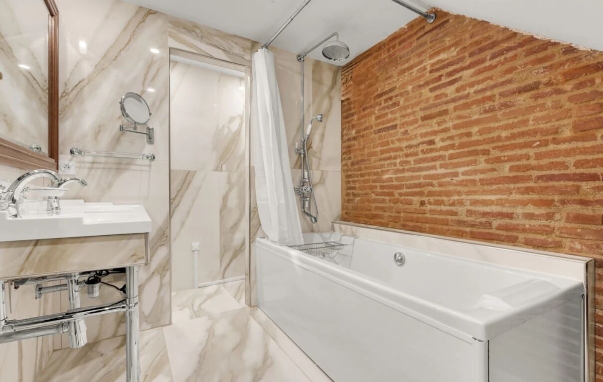 Une salle de bain moderne avec un meuble-lavabo en marbre, une baignoire blanche et un mur d’accent en briques.