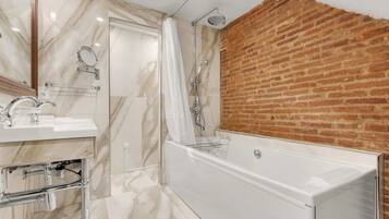 A modern bathroom with a marble vanity, a white bathtub, and a brick accent wall.