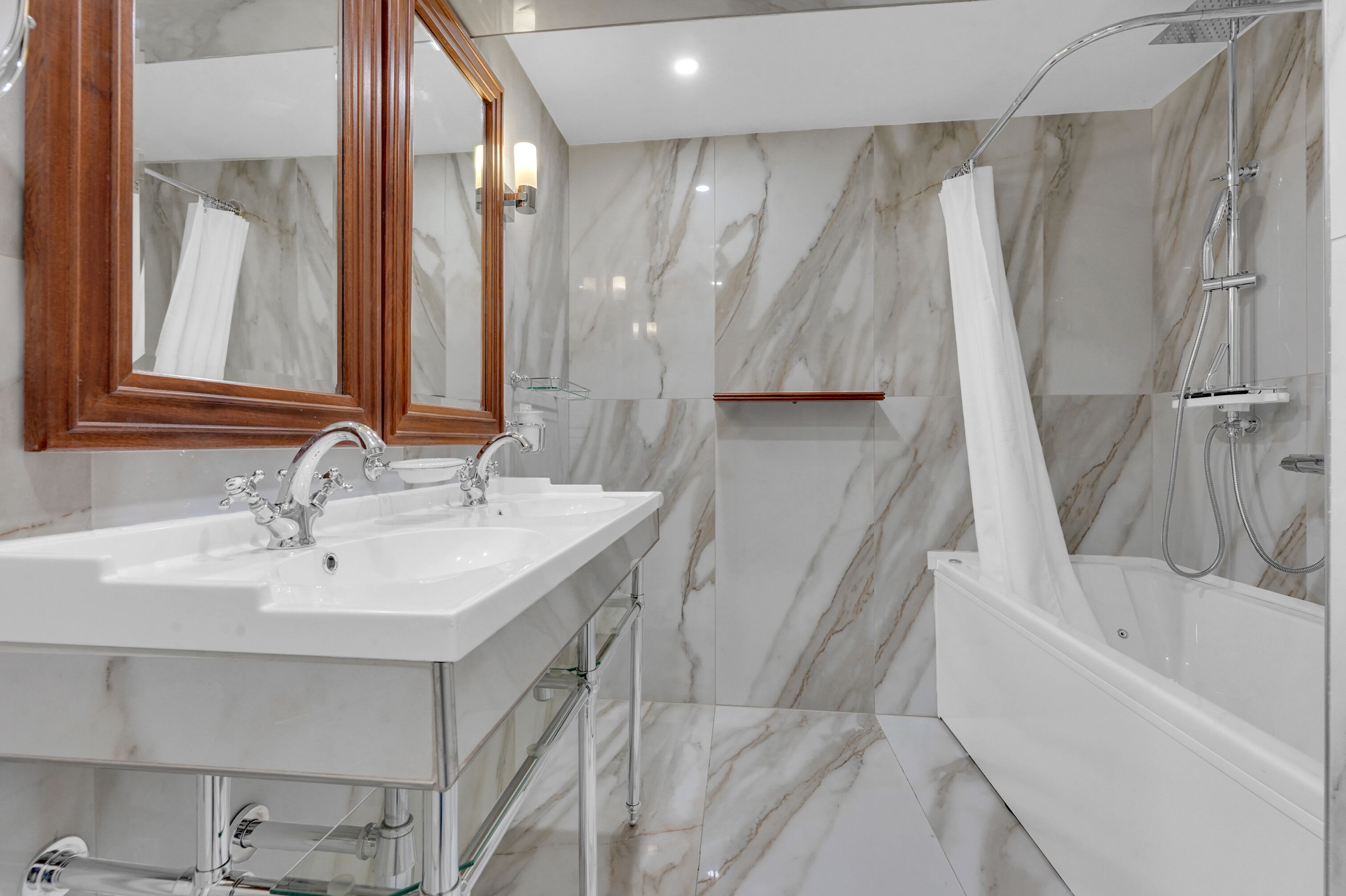 Un baño moderno con paredes de mármol, un espejo grande, dos lavamanos y una ducha a ras de suelo.