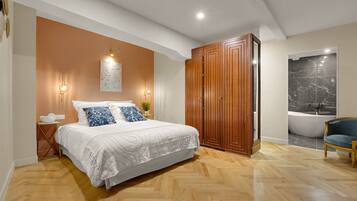 A bedroom with a large bed, wooden wardrobe, and a view of a bathroom with a bathtub.