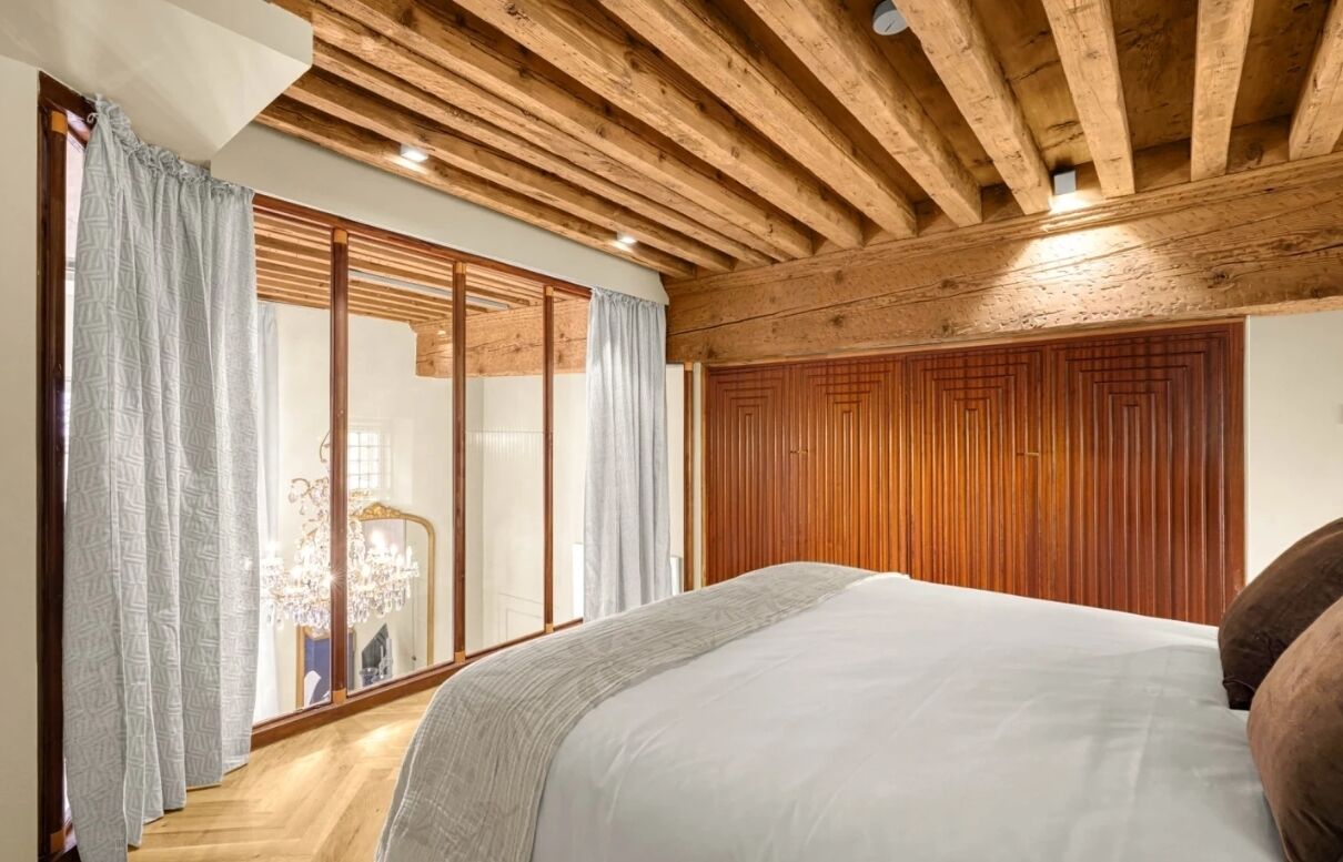 Een slaapkamer met een houten plafond, een groot bed en een schuifdeur naar een balkon.