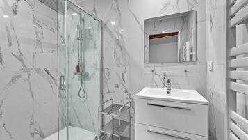 Un baño moderno con ducha de vidrio, lavamanos blanco y paredes de mármol.
