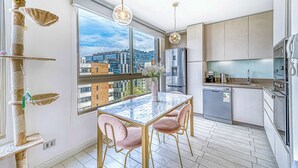 A modern kitchen with a large window, a cat tree, and a dining area with a marble table and pink chairs. - Stylish Art 2B w/ Balcony, Parking & Wifi (Santiago)