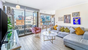 A modern living room with a grey sofa, a pink chair, a round coffee table, and a TV on a glass table. - Stylish Art 2B w/ Balcony, Parking & Wifi (Santiago)