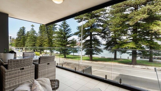 A balcony with wicker furniture and a view of a road and trees. - Stylish Manly Apartment with Harbour Views (Manly)