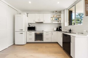 A modern kitchen with white cabinetry, a built-in oven, a microwave, and a dishwasher. - Stylish Manly Apartment with Harbour Views (Manly)