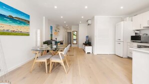 A modern apartment with a dining area, kitchen, and a beach-themed painting on the wall. - Stylish Manly Apartment with Harbour Views (Manly)