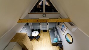 Une pièce de style « loft » avec un plafond en pente, une table à manger avec des chaises, un canapé, un miroir et une horloge au mur.