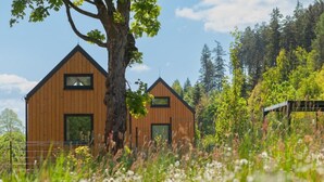 Une cabane en bois, dotée d’un toit à pente, entourée d’un paysage naturel composé d’arbres et de fleurs sauvages.