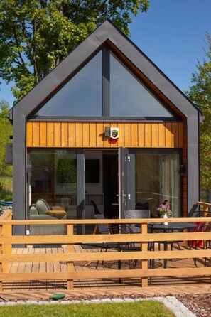 Una cabaña moderna con terraza de madera, ventanas de vidrio amplias y un logo en la puerta.