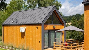 Une cabane en bois avec un toit en pente, une petite terrasse dotée de sièges d’extérieur et une porte d’entrée en verre.