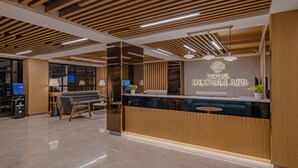 A hotel reception area with a modern design, featuring a wooden reception desk, seating area, and a large mirror reflecting the space. - Treebo Premium D Consulate (Hyderabad)