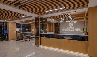 A hotel reception area with a modern design, featuring a wooden reception desk, seating area, and a large mirror reflecting the space.