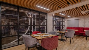 A modern dining area with large windows, wooden ceiling, and red upholstered seating. - Treebo Premium D Consulate (Hyderabad)