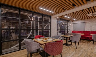 A modern dining area with large windows, wooden ceiling, and red upholstered seating.