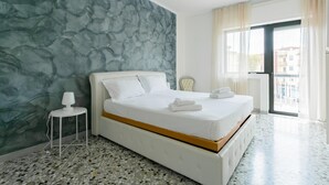 A modern hotel room with a large bed, a small side table, a lamp, and a view of the city through the window. - Casa Campione by Wonderful Italy (Bari)