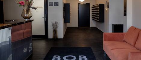 A reception area with a reception desk, a black rug with "BOB W." on it, a sofa, a wall-mounted display, and a door leading to another room.