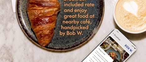 A croissant on a plate with a cup of coffee and a smartphone displaying a breakfast menu.