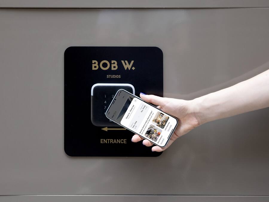 A hand holding a smartphone with a hotel entrance sign displaying "BOB W. STUDIOS" and an arrow pointing to the entrance.