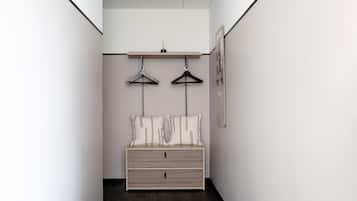A narrow hallway with a bed at the end, a hanging shelf above, and a framed picture on the wall.