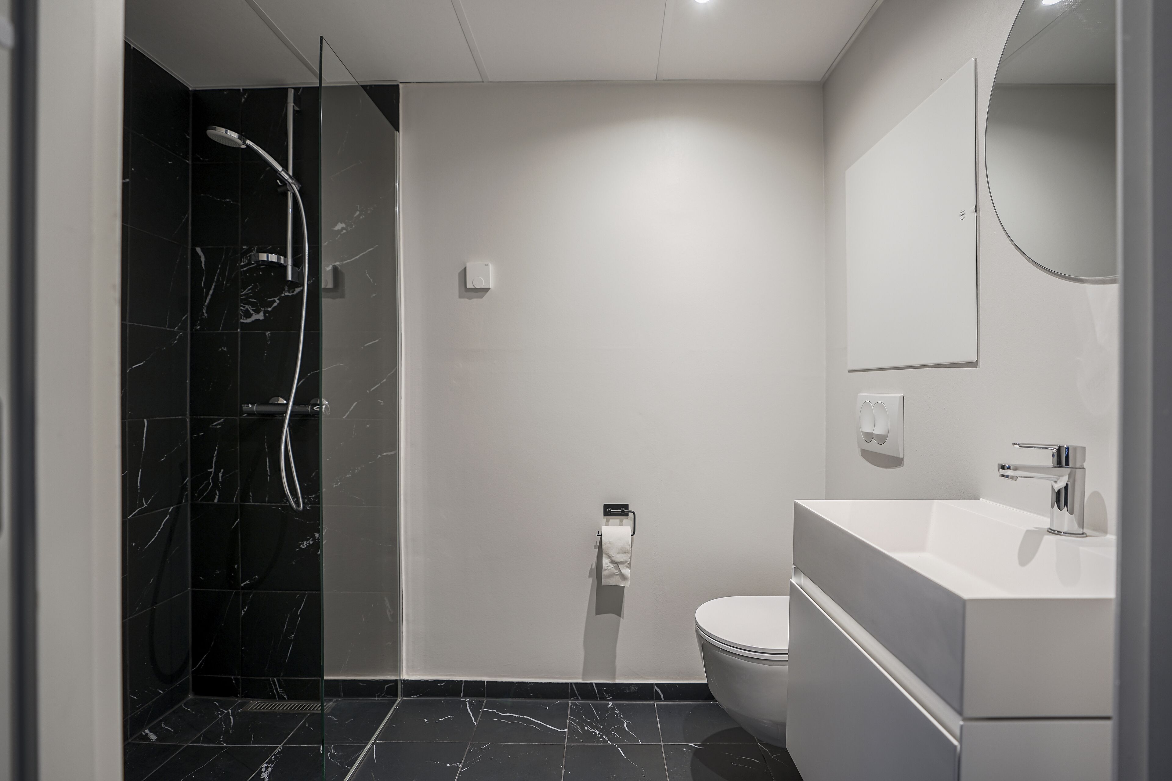Un baño moderno con ducha de vidrio, inodoro y lavamanos con espejo.
