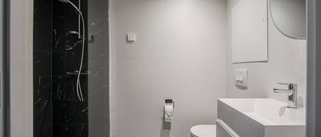 Un baño moderno con ducha de vidrio, inodoro y lavamanos con espejo.